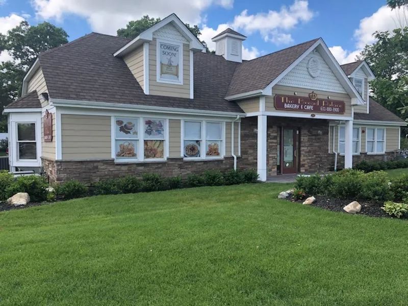 Cream-colored building with brown roof, stone base, and well-maintained lawn. Sign says 