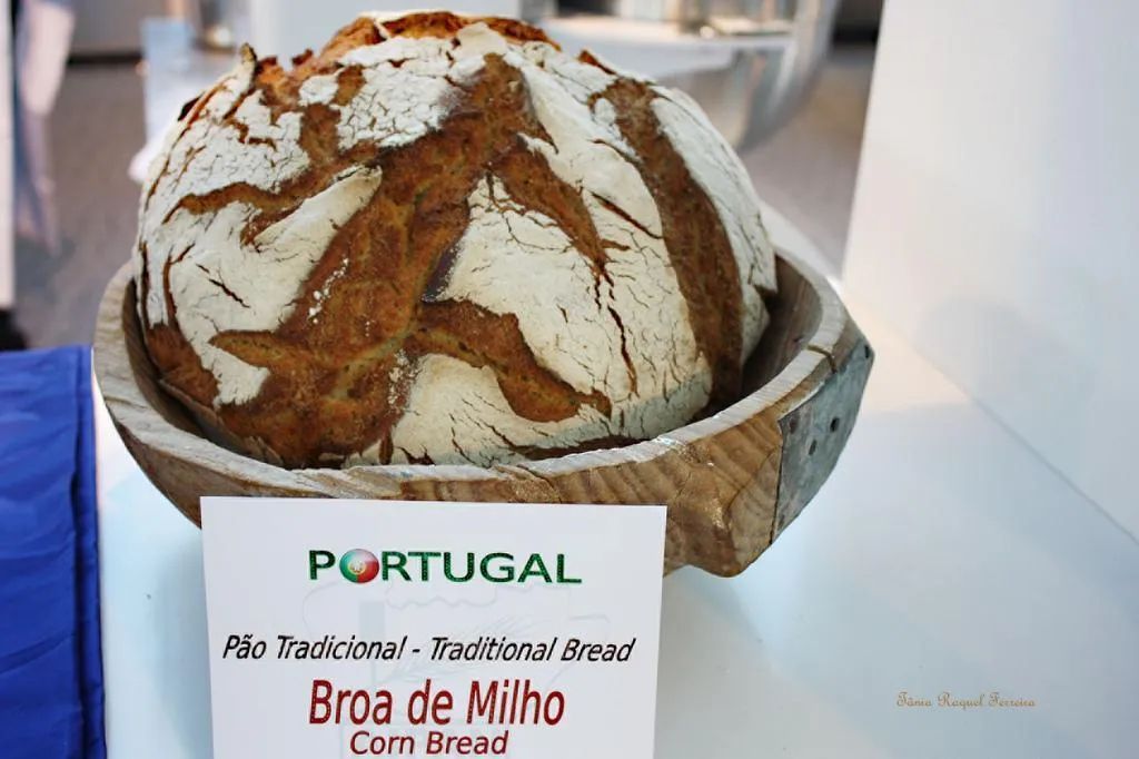 Round loaf of Broa de Milho corn bread in a wooden bowl, labeled 