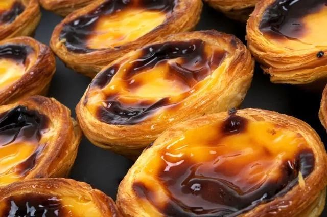 Close-up of several golden-brown Portuguese custard tarts with caramelized tops, in a dark setting.