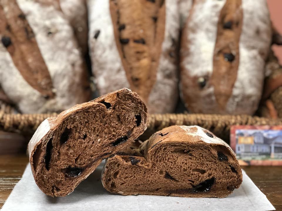 Sliced chocolate bread with whole loaves in the background, on a wooden table.