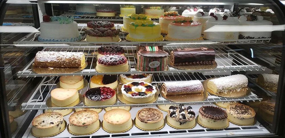 Display case filled with various cakes, including cheesecakes and layered pastries.