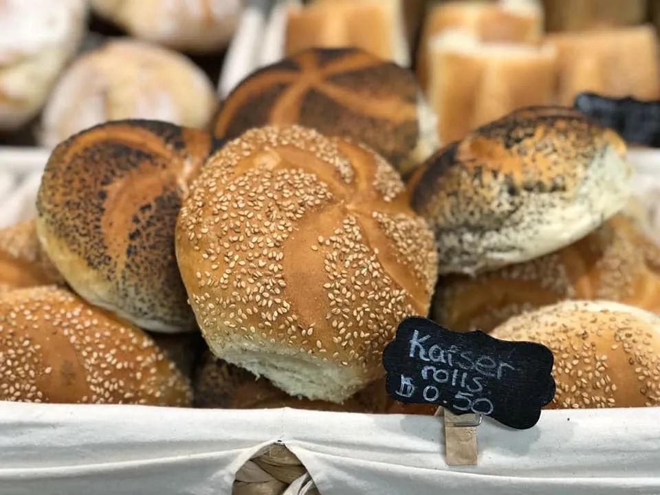 Kaiser rolls in a basket, some with sesame seeds. A sign reads 