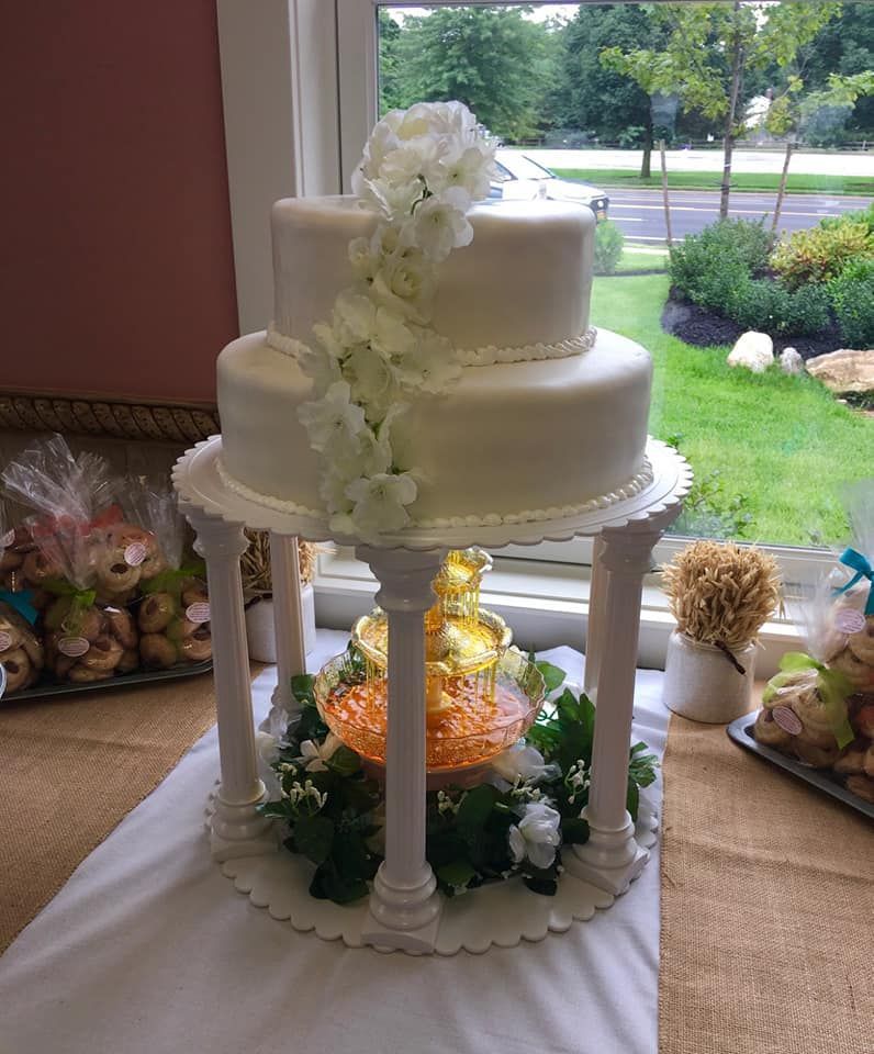 Three-tier white cake with floral accents, supported by pillars, with a fountain below.