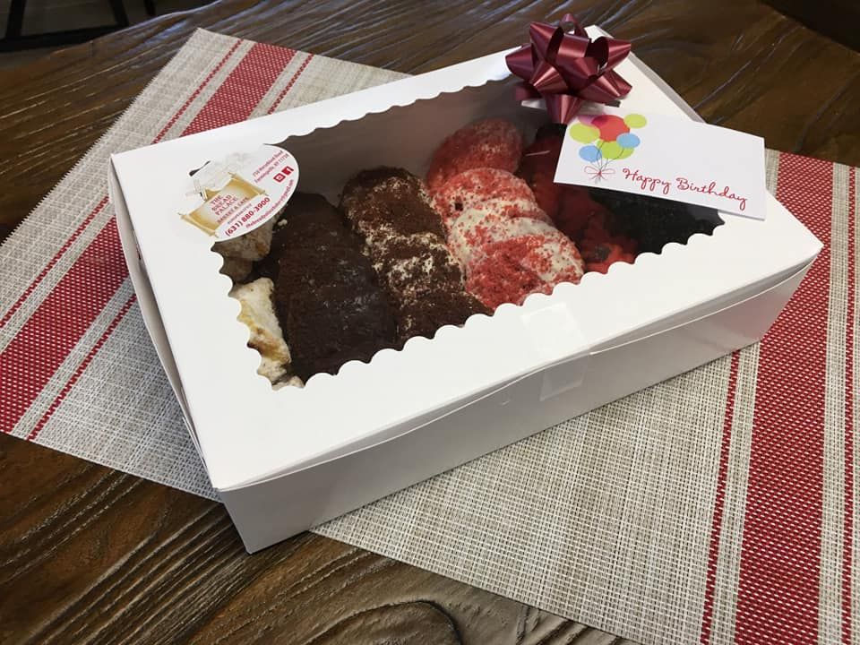 Boxed eclairs with various toppings, birthday card, and bow on a striped placemat.