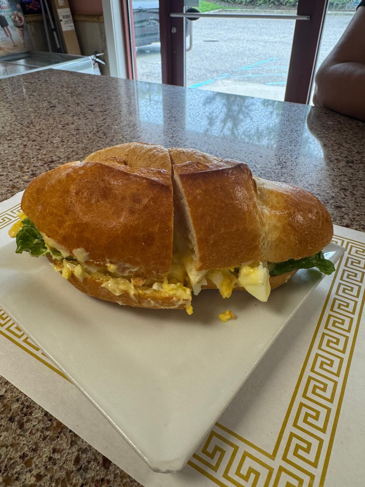 Egg salad sandwich, cut in half, on white plate with gold pattern, indoors.