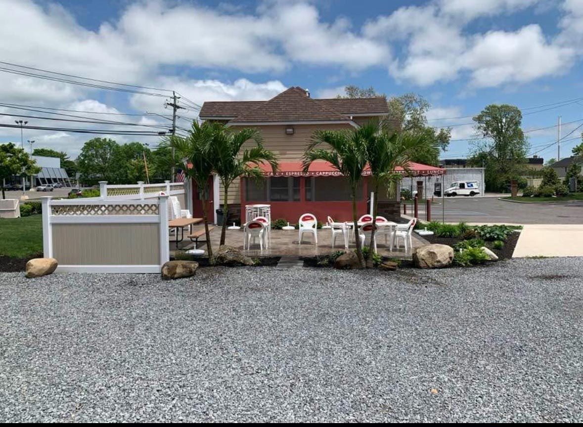 Outdoor patio with gravel, chairs, palm trees, and a building under a cloudy sky.