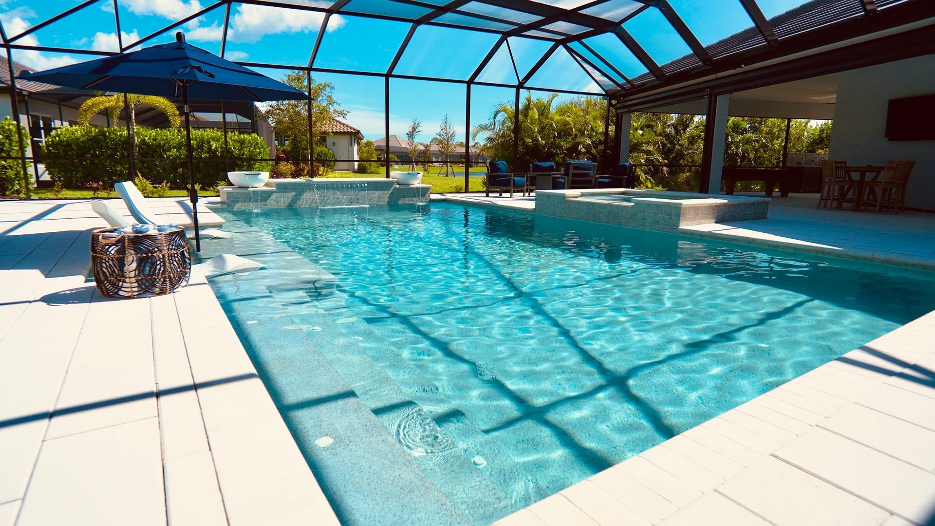 Pool with clear blue water and spa, under screened enclosure, patio, and blue umbrella.