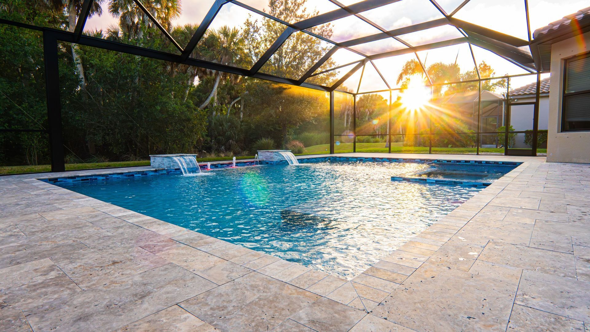 Pool with cascading water features, screened enclosure, and sunset backdrop.