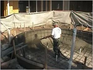 Man spraying concrete inside a pool under construction.