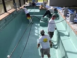 Workers repaint an empty, turquoise-colored swimming pool.