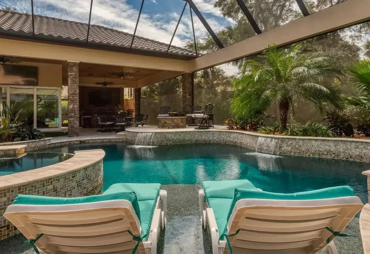 Two teal lounge chairs face a turquoise pool with a waterfall feature, under a covered patio.