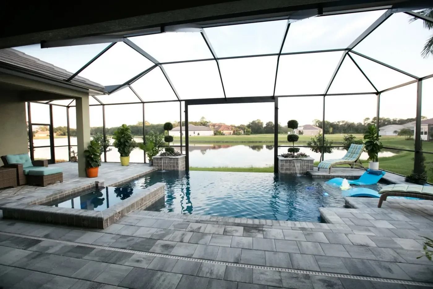 Screened-in pool area with lake view. Pool, spa, lounge chairs, and landscaping under a geometric screen enclosure.