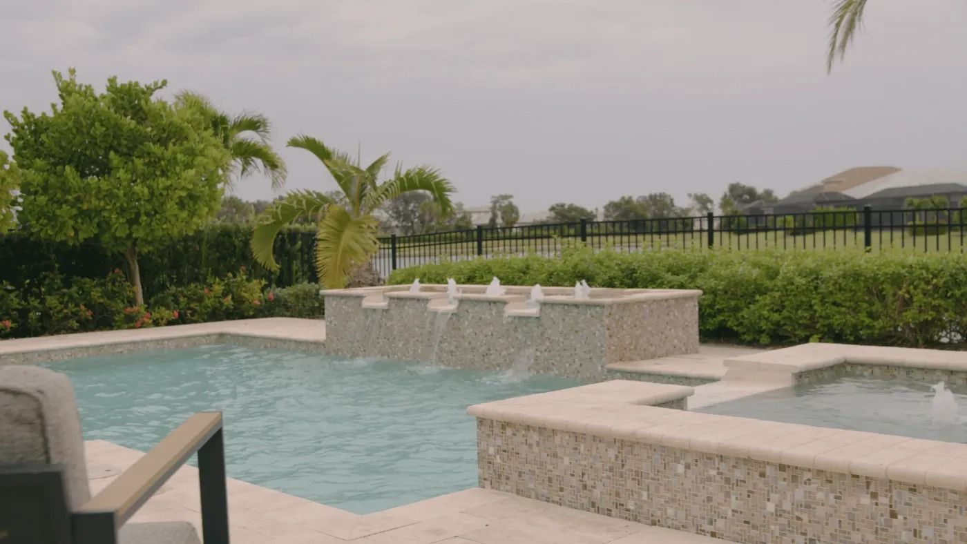 Swimming pool with water fountains, surrounded by landscaping and a fence.