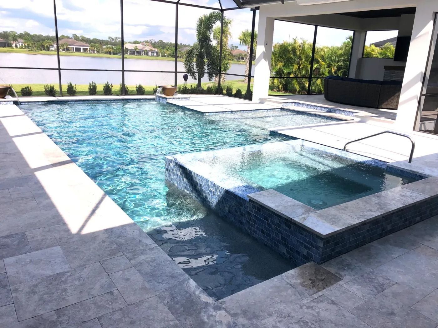 Pool with a raised spa, light blue tiles, lake view, sunny day.