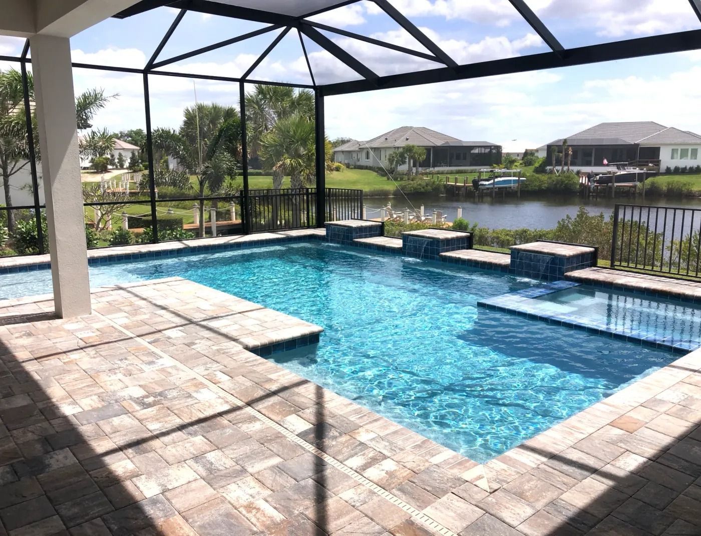 Pool with blue water and waterfalls, surrounded by a screened patio and overlooking a lake.