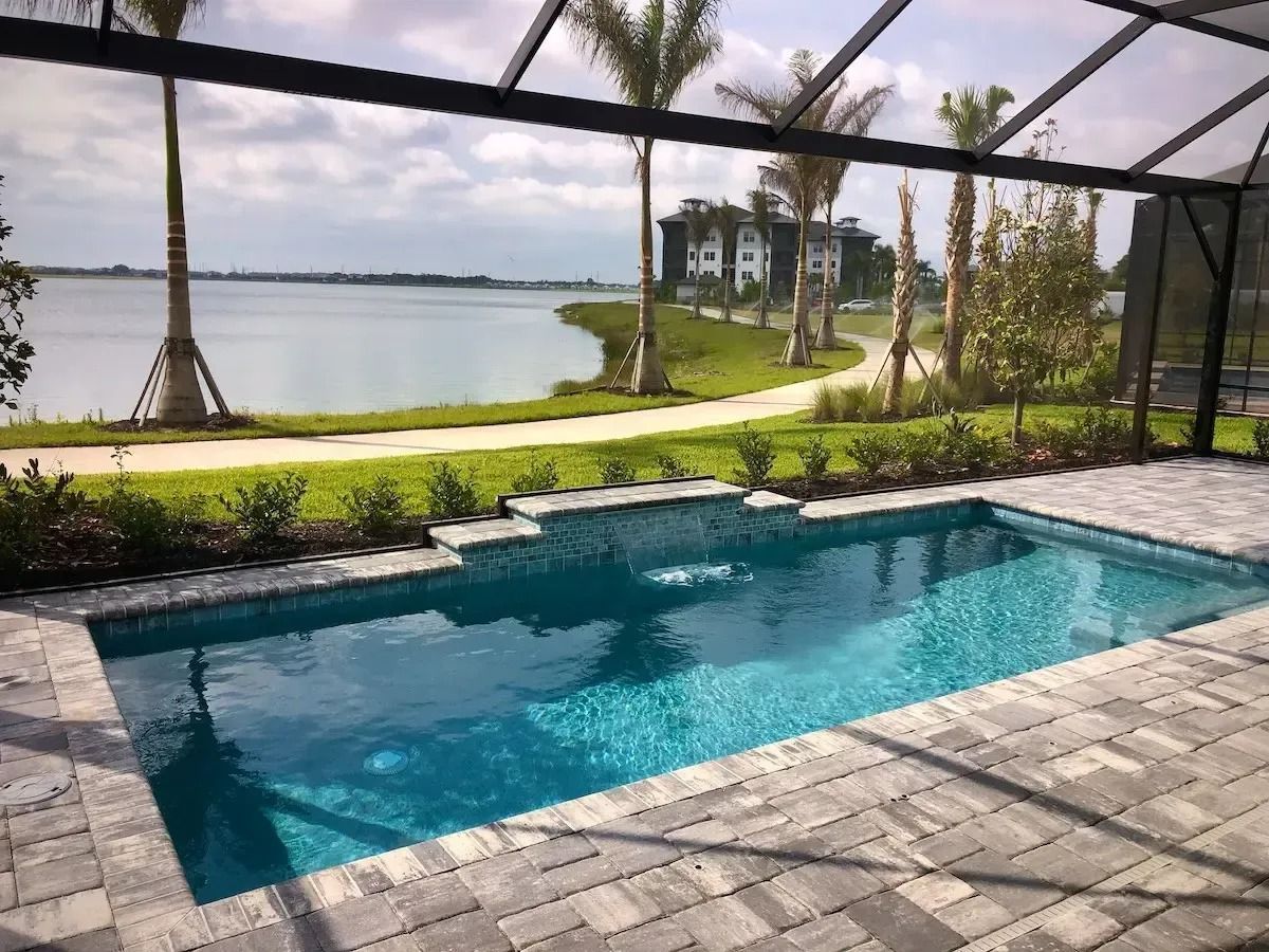 Pool overlooking a lake, surrounded by greenery and palm trees. Sunny day with blue water and sky.