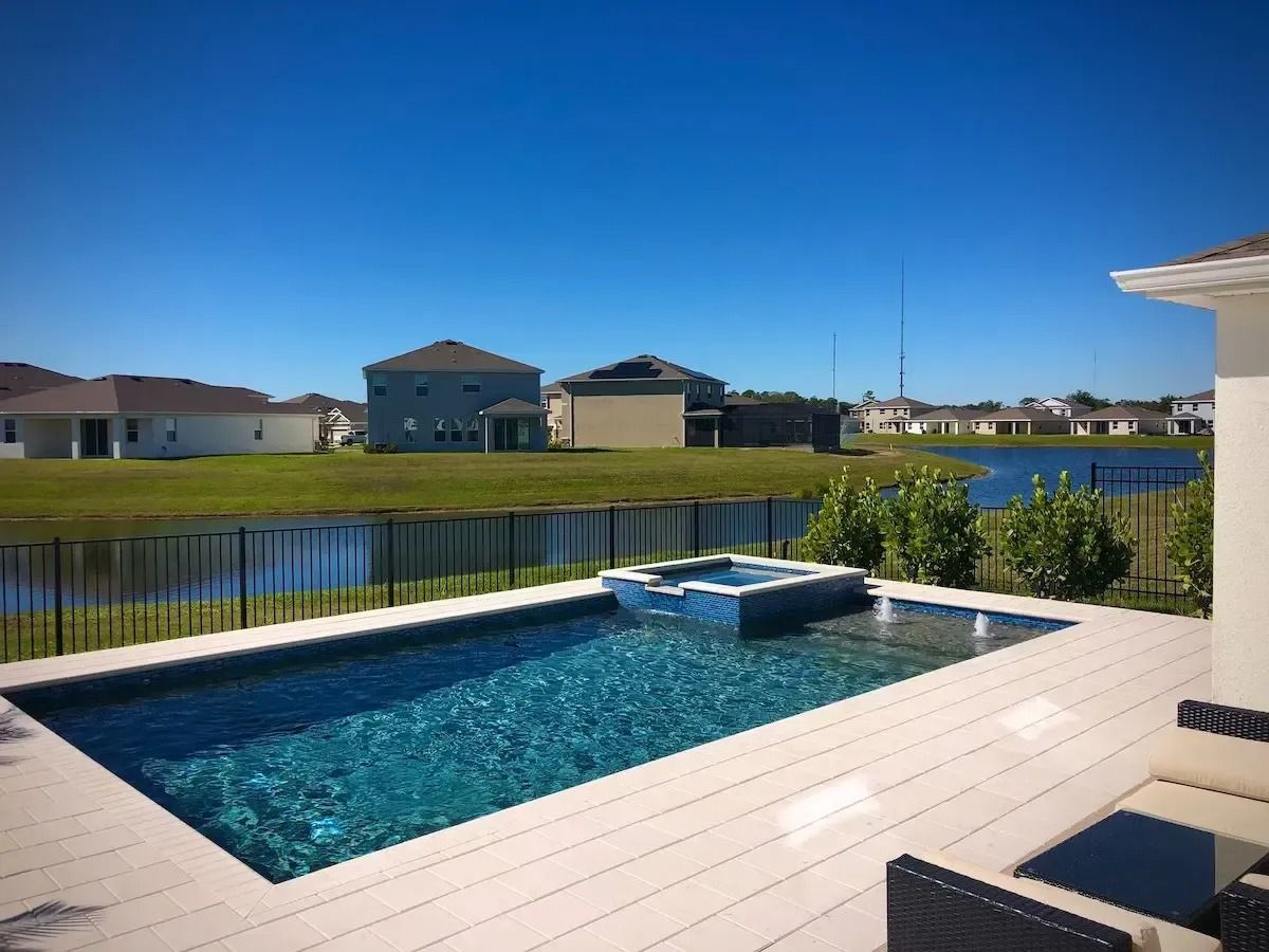 Backyard pool overlooking a lake and houses under a clear blue sky.
