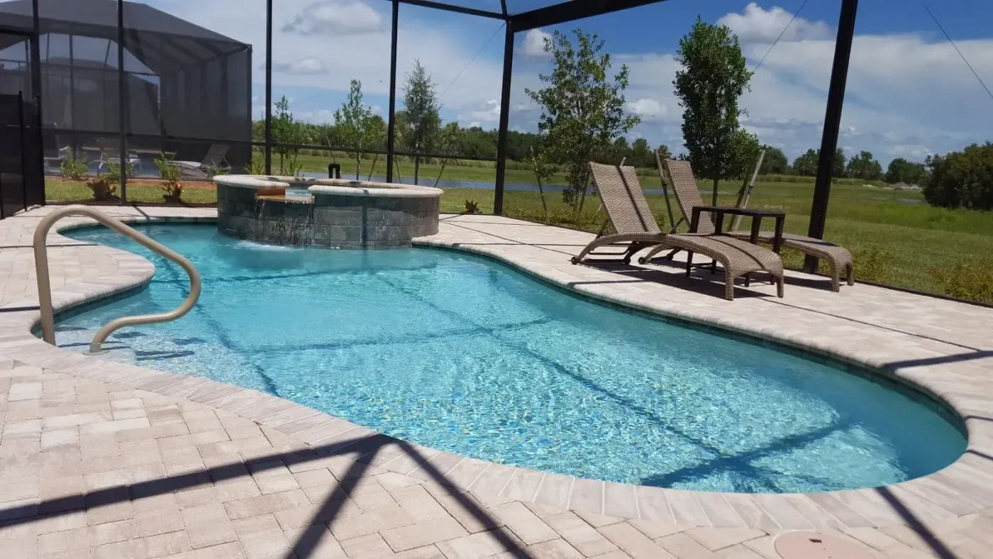 Pool with spa, waterfall, and lounge chairs under a screened enclosure; sunny outdoor setting with grass and trees.