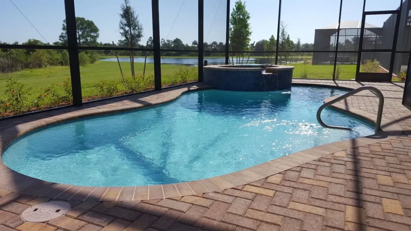 Pool with attached spa, surrounded by screen enclosure, brick patio, and grassy landscape.