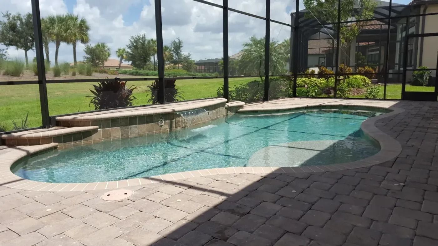 A small, blue-tiled pool with a waterfall feature surrounded by a brick patio and screen enclosure.
