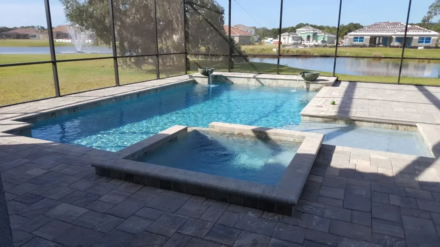 Pool and spa with water and patio, with a lake and houses in the background.