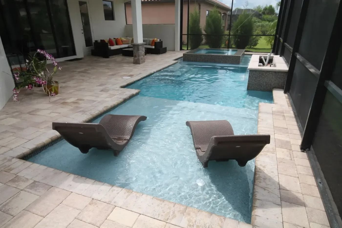 Outdoor pool with two submerged lounge chairs, hot tub, and patio area.