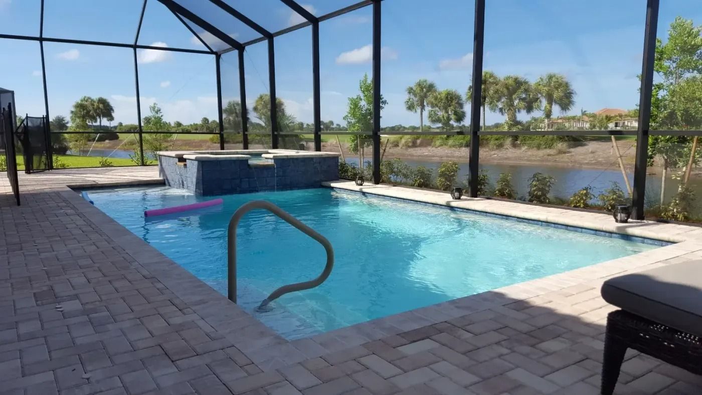 Pool with screen enclosure, brick patio. Blue water, handrail, and spa. View of lake and trees.