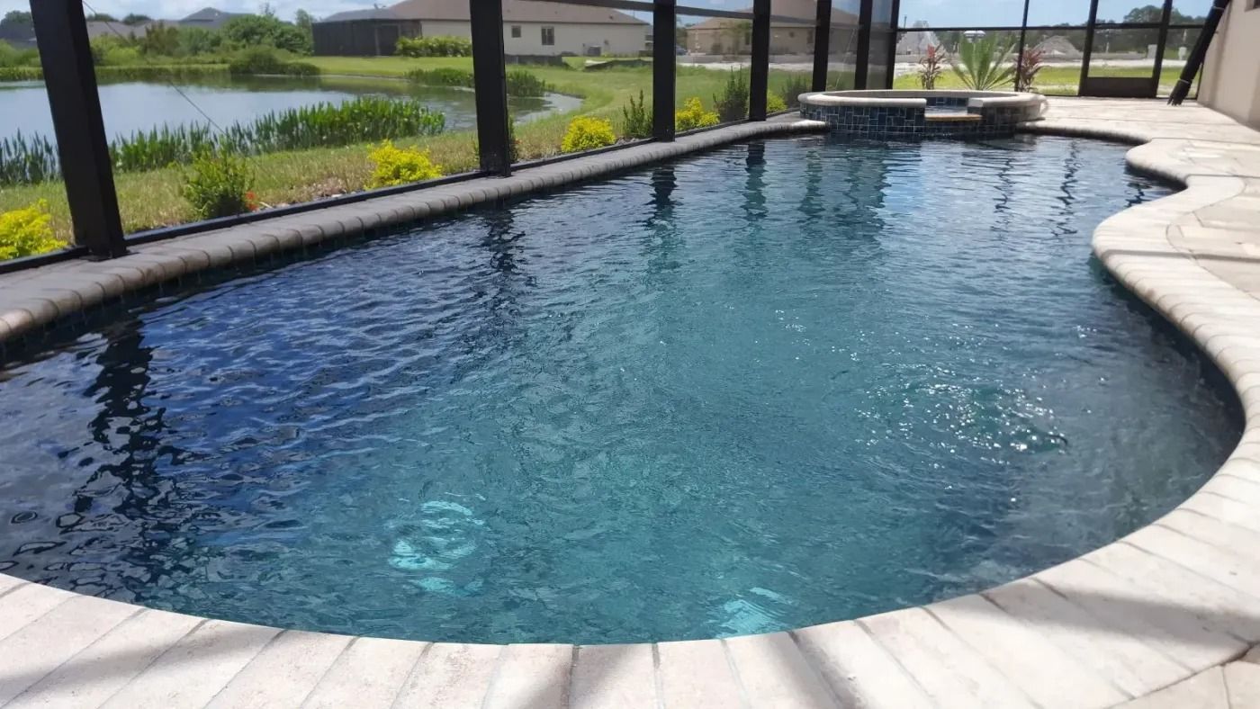 Swimming pool with dark blue water surrounded by stone patio, screened enclosure, and pond.