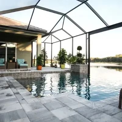 A swimming pool with screened enclosure next to a body of water.