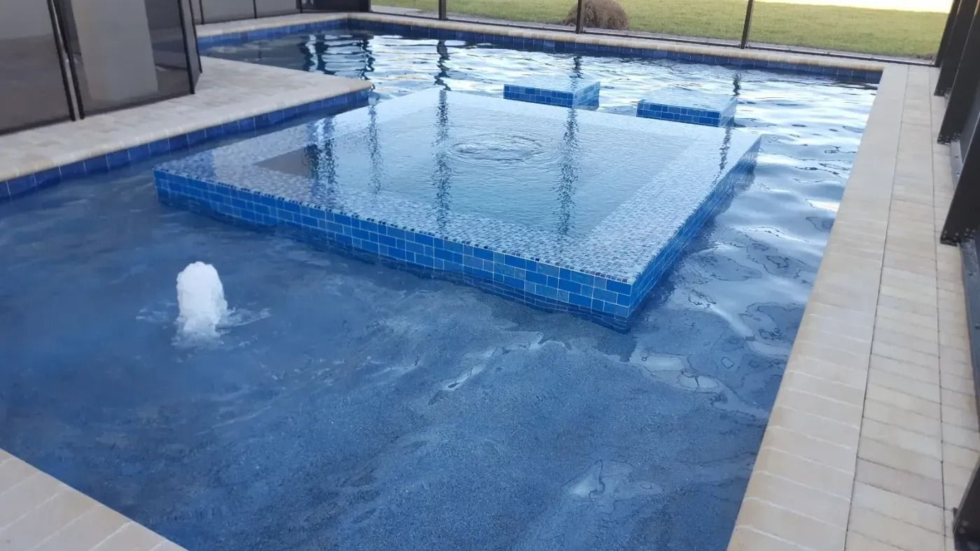 Pool with blue mosaic tiles, water fountain, and raised square structure.