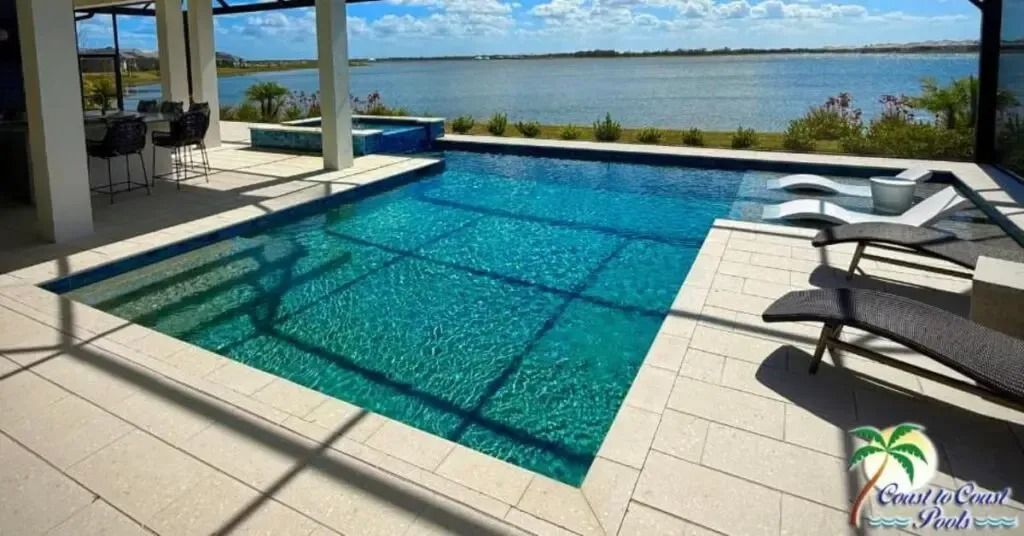Pool with teal water, surrounded by beige tiles, overlooking a large body of water.