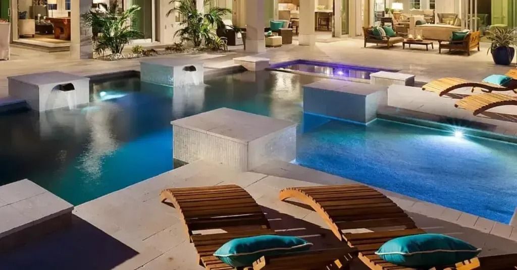 Pool area with wooden lounge chairs, illuminated floating blocks, and lush greenery.