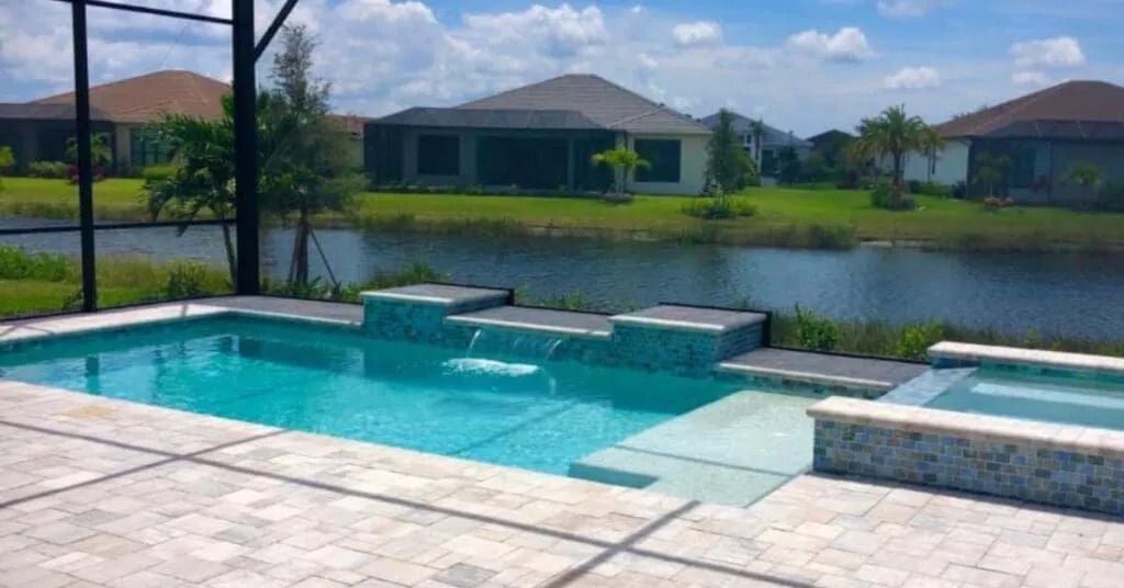 Swimming pool with water features, steps, and jacuzzi overlooking a lake and houses.