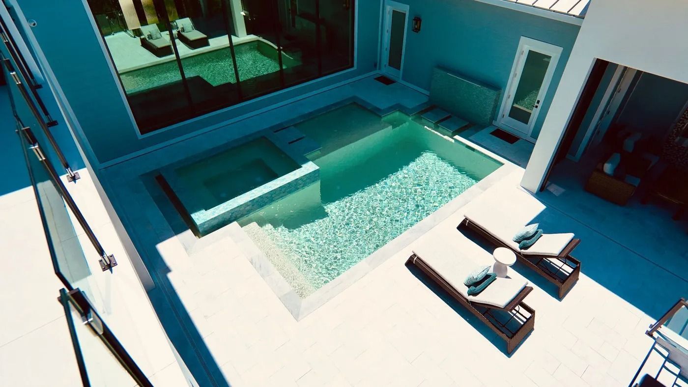High-angle view of a backyard with a pool, hot tub, and lounge chairs on a sunny day.
