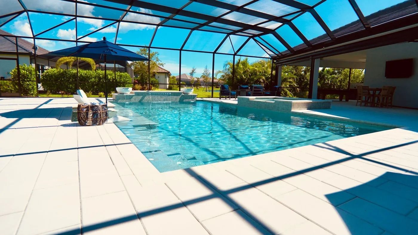 Swimming pool enclosed in a screened patio, bright blue water, and white tiled deck under a sunny sky.