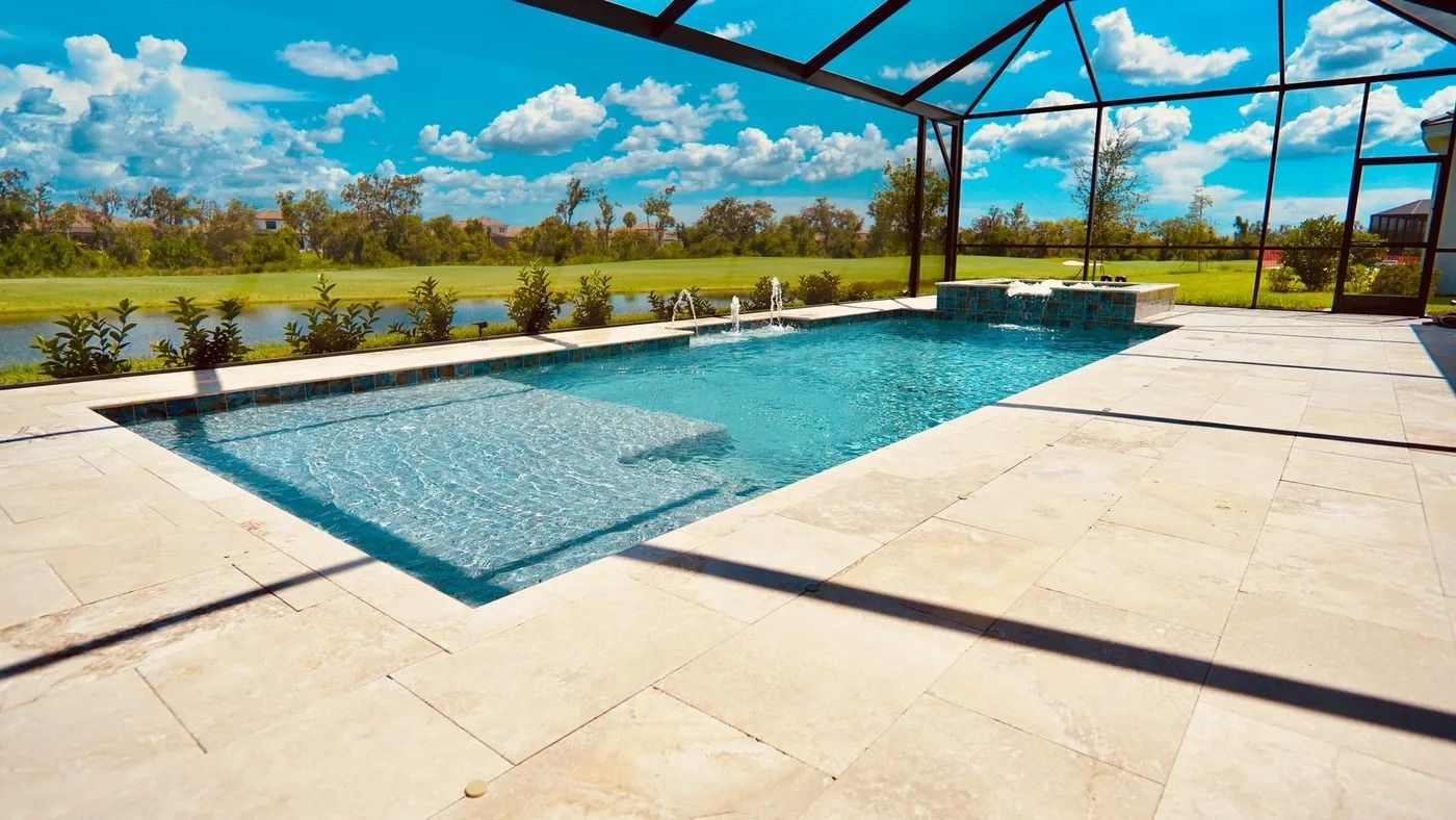 Swimming pool with clear blue water and stone patio under a screened enclosure with a sunny sky background.