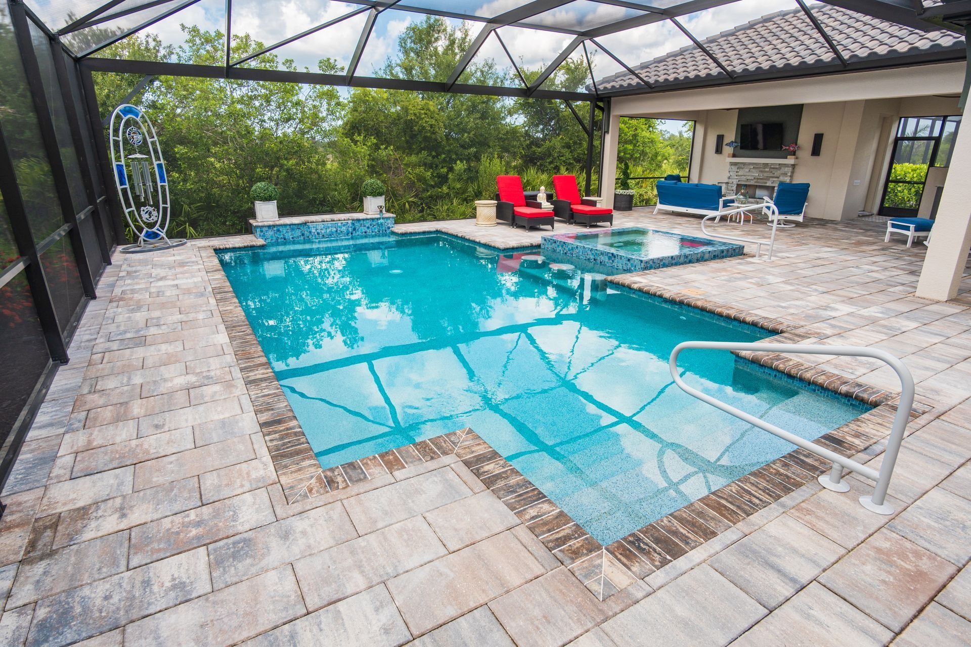 Covered backyard pool with blue water, brick deck, red loungers, and a pavilion with seating