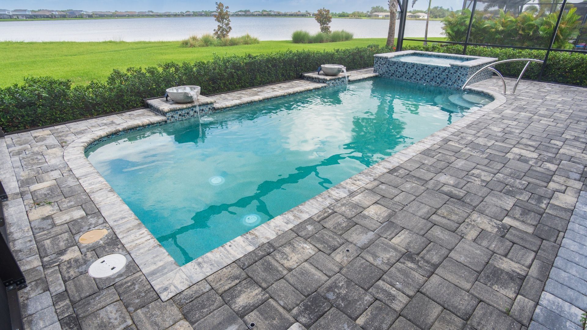 Rectangular backyard pool with turquoise water, stone patio, and lake view beyond the lawn
