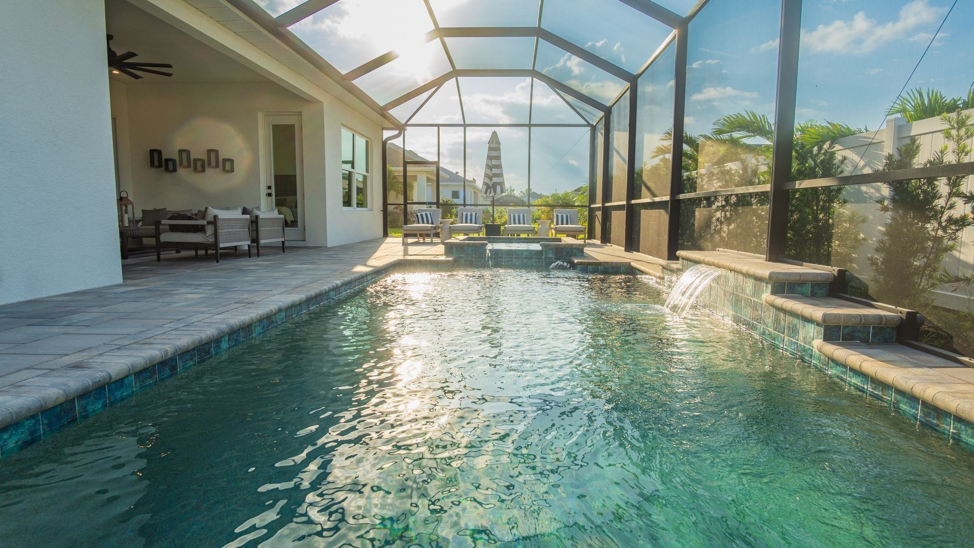 Covered backyard pool with clear water, screened patio, lounge chairs, and ocean view beyond the glass enclosure