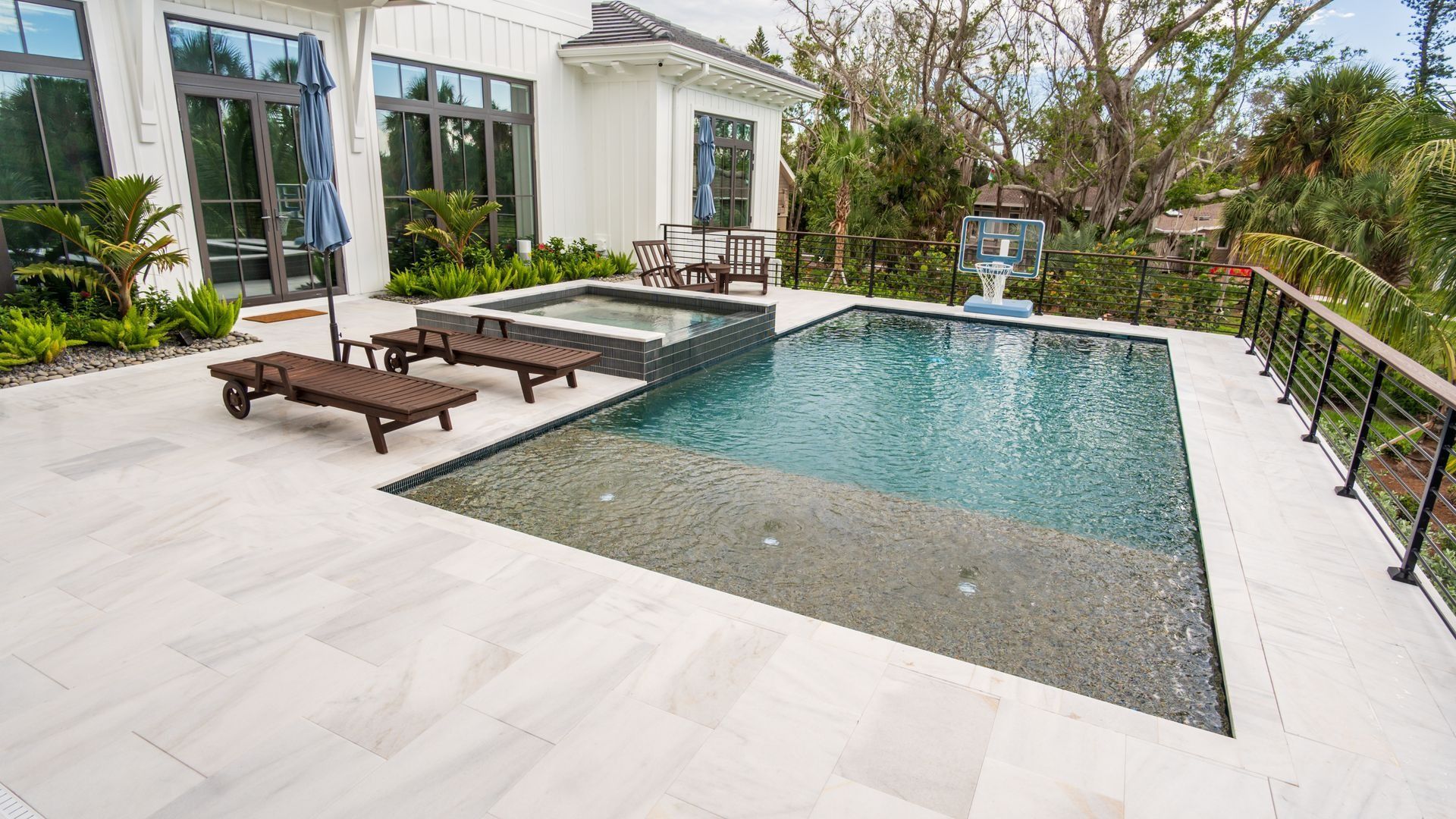 Modern backyard pool with lounge chairs, white patio, and tropical landscaping