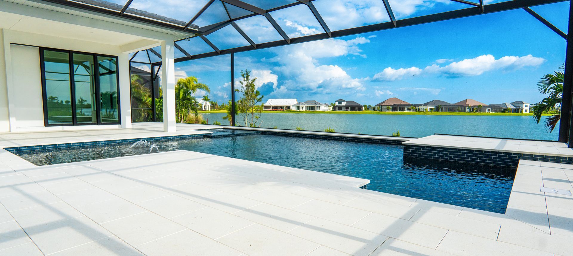 Modern patio with infinity pool, glass canopy, and waterfront view under a bright blue sky