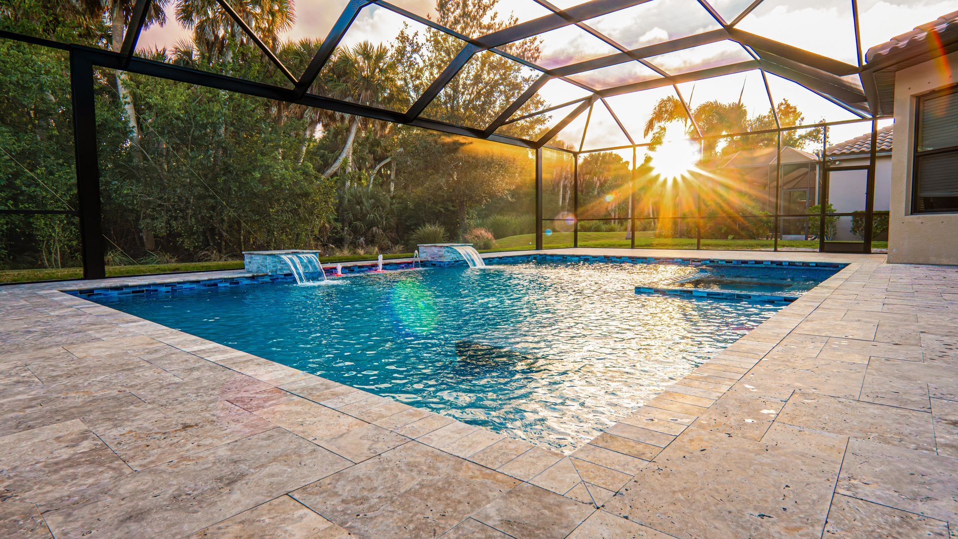 Sunlit backyard pool with blue water, stone deck, and screened enclosure at sunset