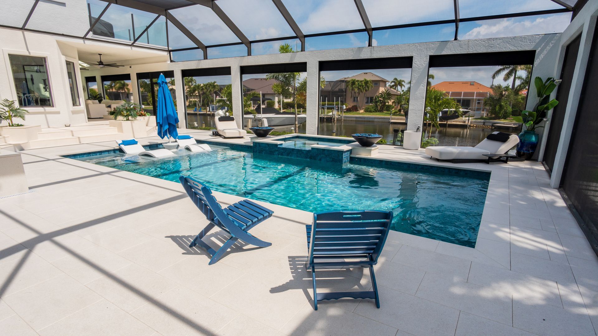 Screened-in patio with a swimming pool, lounge chairs, and a blue umbrella under a bright sky