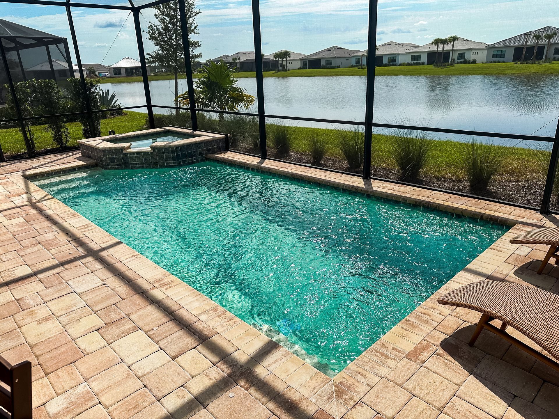 Screened backyard pool beside a lake, with tan pavers and lounge chairs