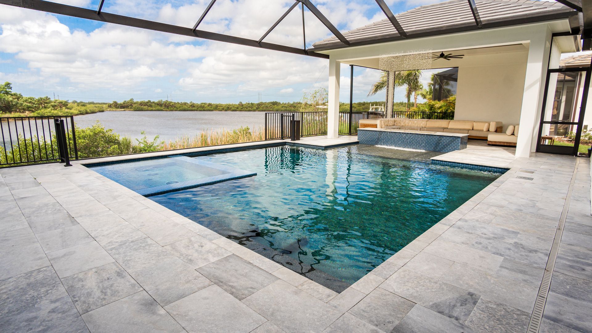 Covered outdoor pool beside a patio overlooking a lake, with clear blue water and stone decking