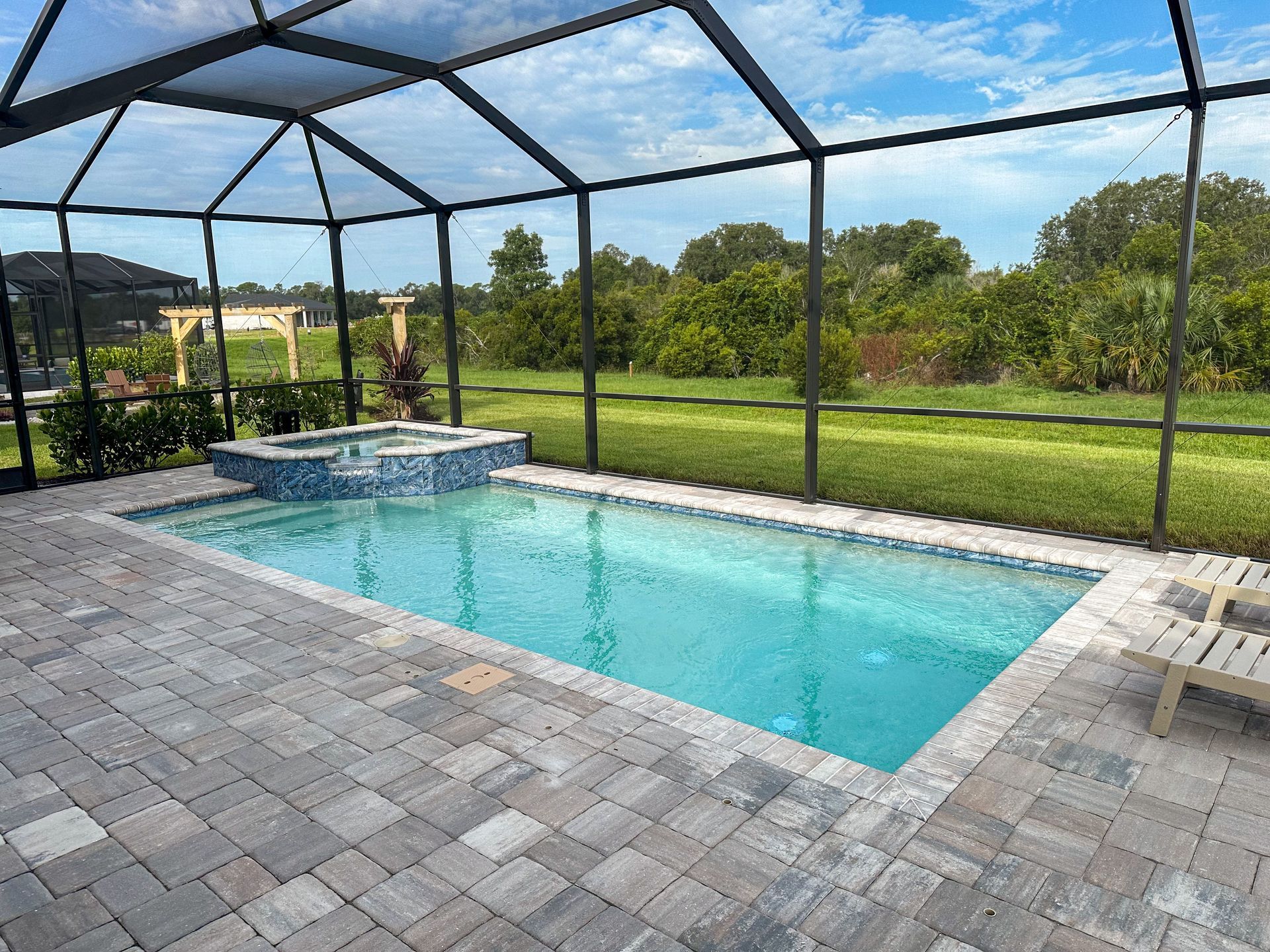 Screened backyard pool with blue water, stone patio, and grassy lawn beyond.
