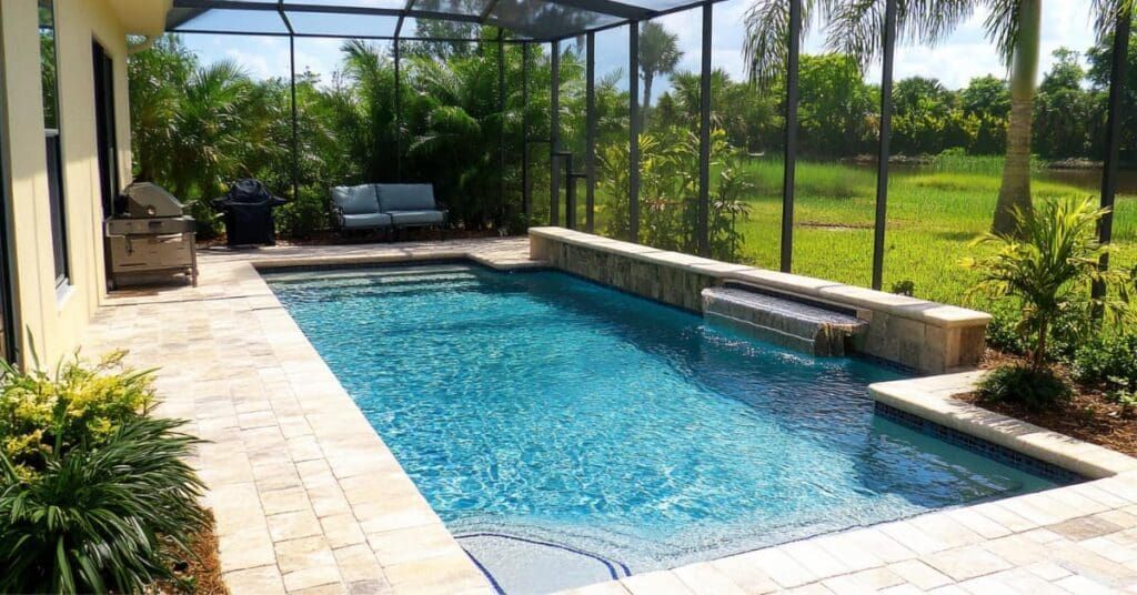 Rectangular swimming pool with a waterfall, surrounded by beige patio and screened enclosure.
