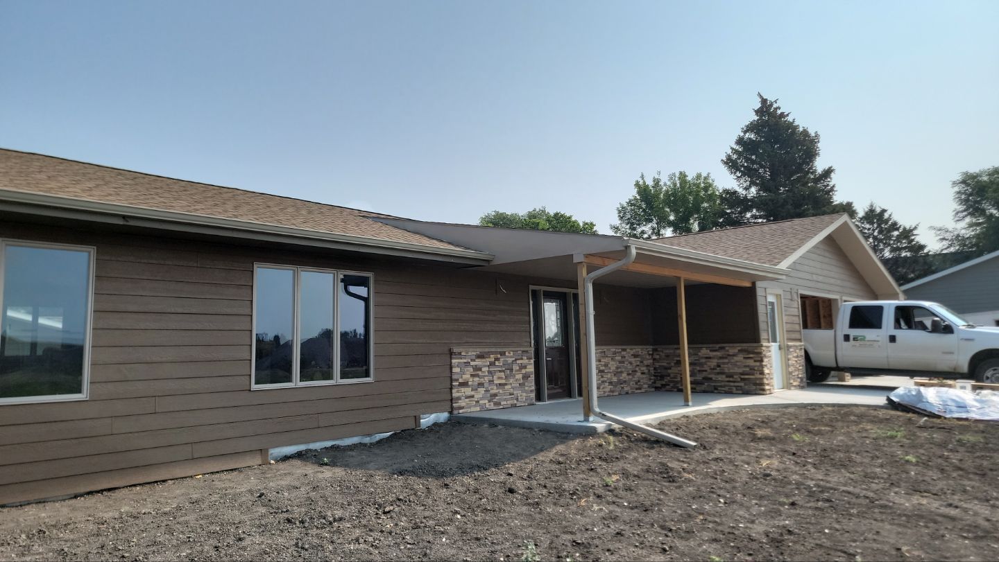 A newly constructed house with brown siding and a covered entryway. A white truck is parked nearby.