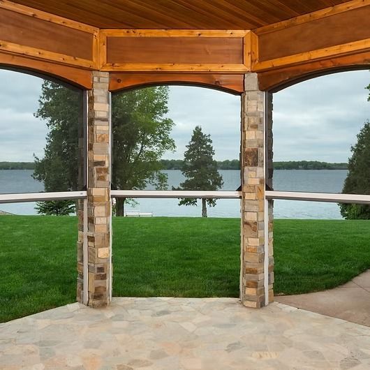 Gazebo with stone columns and a view of a lake and green lawn under an overcast sky.