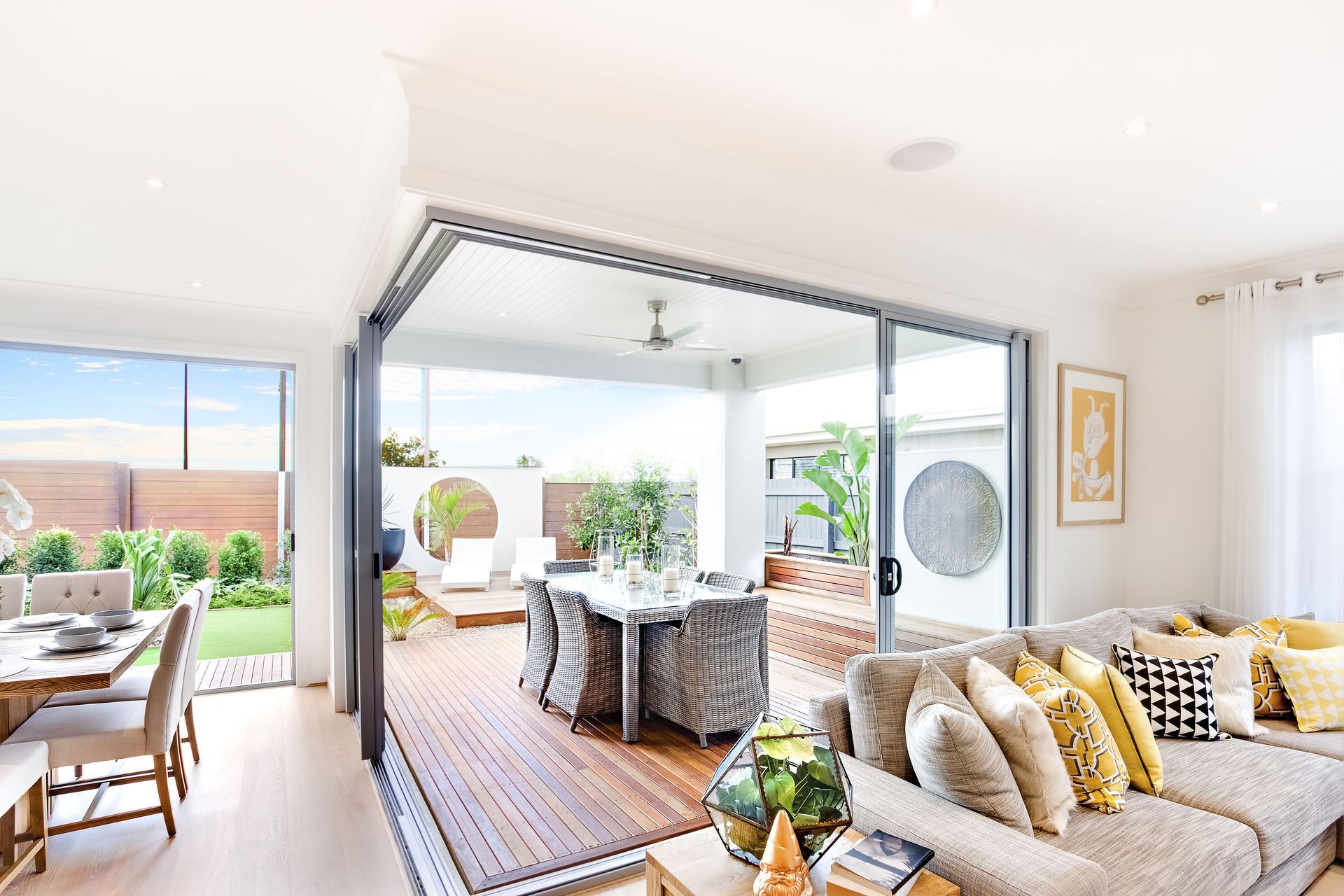 Living room with open sliding doors to a patio. Includes a dining area, seating, and outdoor dining.